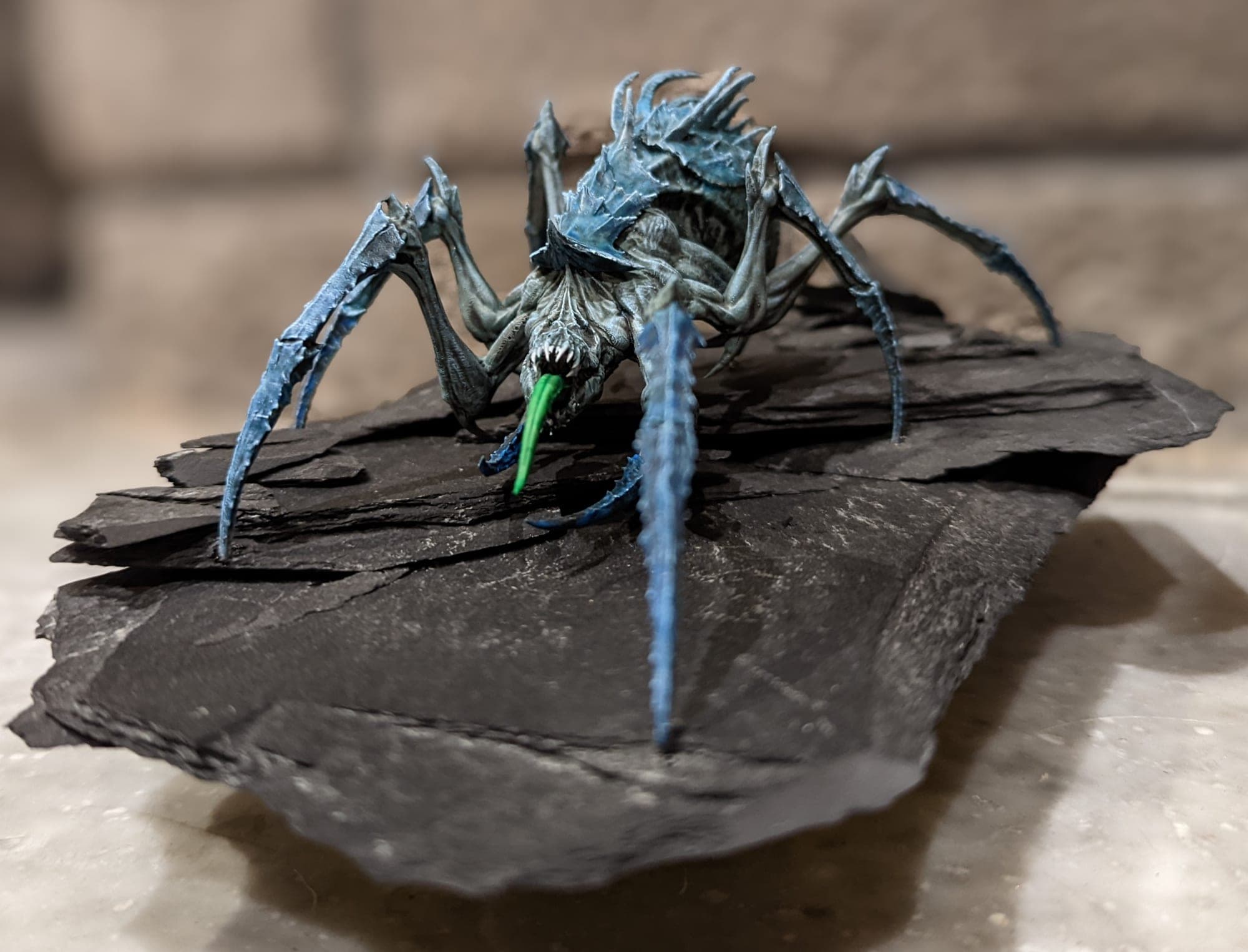 Blue spider-like creature posed on a slate base